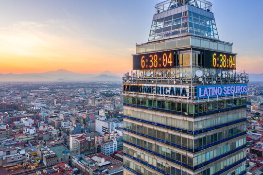 Aerial view of Torre Latinoamericana with its digital clock glowing at sunset, overlooking the dense urban sprawl and distant mountains of Ciudad de Mexico, Ciudad de Mexico, Mexico.