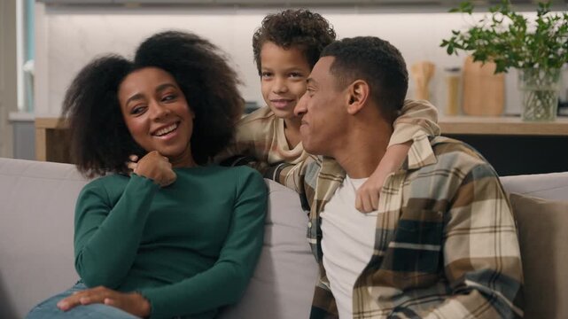 Happy African American family parents mother father cuddling little boy child son having fun talking dad mom kid togetherness adoption custody childcare indoors cozy modern apartment home lifestyle