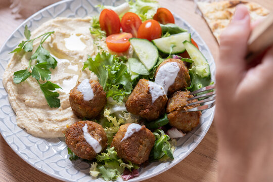 Person holding plate of falafel with hummus and fresh salad. Close up
