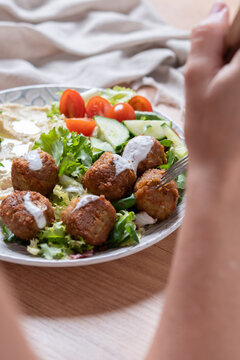 Person holding plate of falafel with hummus and fresh salad. Close up