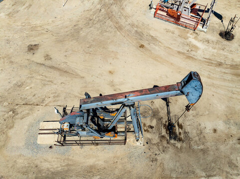 Aerial view of oil pump jacks operating in a dry, sandy field under bright sunlight in Bakersfield, California, United States.