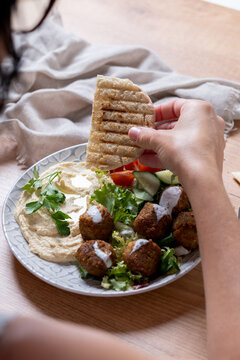 Person holding plate of falafel with hummus and fresh salad. Close up