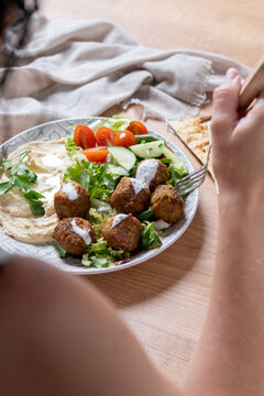 Person holding plate of falafel with hummus and fresh salad. Close up