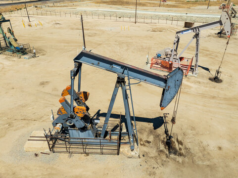 Aerial view of oil pump jacks operating in a dry, sandy landscape in Bakersfield, California, United States.