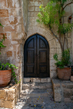Old wooden door in a stone wall with plants around in Lindos