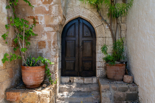 Old wooden door in a stone wall with plants around in Lindos