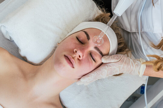 Cosmetologist using frequency darsonval device for skin rejuvenation, acne treatment, and anti-aging therapy in a modern medical spa.