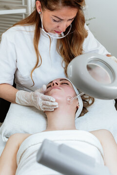 Cosmetologist using frequency darsonval device for skin rejuvenation, acne treatment, and anti-aging therapy in a modern medical spa.