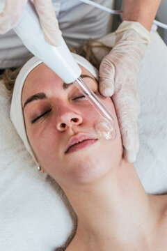 Cosmetologist using frequency darsonval device for skin rejuvenation, acne treatment, and anti-aging therapy in a modern medical spa.