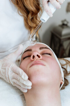 Cosmetologist using frequency darsonval device for skin rejuvenation, acne treatment, and anti-aging therapy in a modern medical spa.