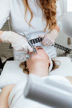 Professional skincare specialist using an airbrush tool to administer oxygen facial hydrating serum on a client during a rejuvenating spa procedure.