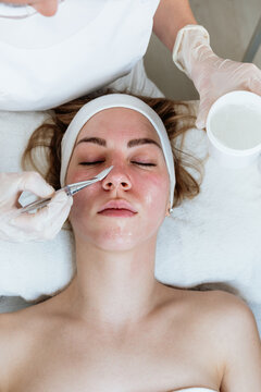 Cosmetologist applying exfoliating mask with brush on client's face during rejuvenating skincare procedure in wellness salon.