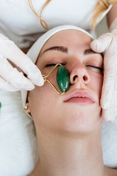 Rejuvenating skin care session at wellness clinic, receiving facial massage with traditional gua sha jade roller tool for health and beauty.