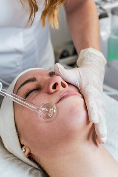 Cosmetologist using frequency darsonval device for skin rejuvenation, acne treatment, and anti-aging therapy in a modern medical spa.