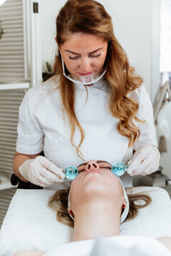 Relaxing skincare treatment session in a modern beauty salon, featuring client receiving refreshing cold globe therapy from an expert therapist.
