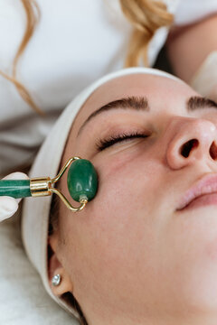 Rejuvenating skin care session at wellness clinic, receiving facial massage with traditional gua sha jade roller tool for health and beauty.