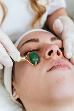 Rejuvenating skin care session at wellness clinic, receiving facial massage with traditional gua sha jade roller tool for health and beauty.