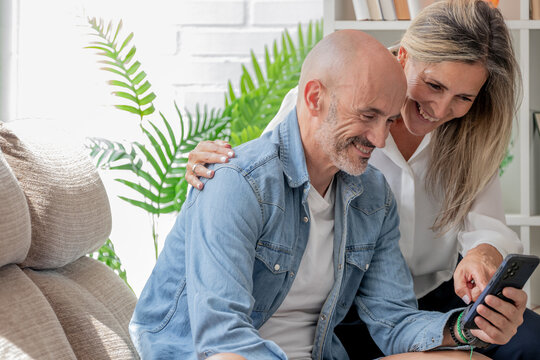 Happy caucasian couple at home sharing a joyful moment on the sofa, looking at a smartphone screen together