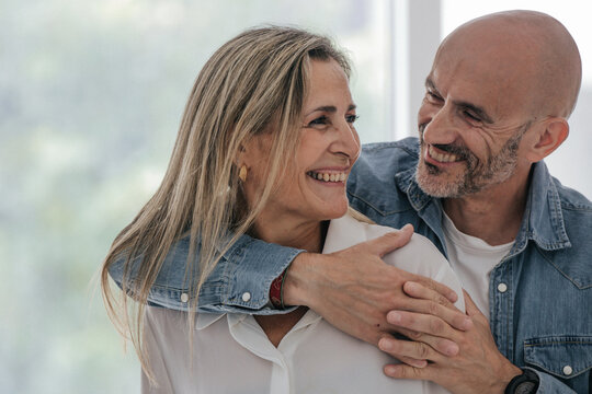 Cheerful middle-aged caucasian couple sharing a warm embrace indoors, radiating love, happiness, and togetherness in a bright, modern home setting