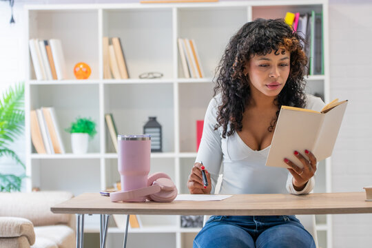young african american woman reading book and taking notes at home library