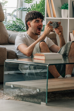 Young person or student sitting in the living room of home playing excitedly online with mobile phone or smartphone