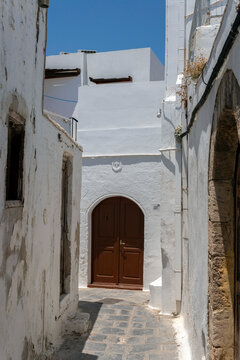 Narrow pathway between white buildings with a wooden door under a blue sky in Lindos