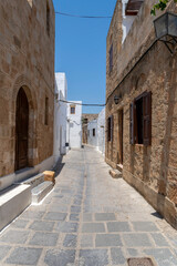 Obraz premium Narrow stone street between old buildings in Lindos under a clear blue sky