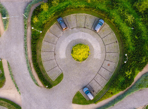 Aerial view of a circular parking lot with cars parked in designated spaces, surrounded by lush green hedges and a central tree in Sopot, Wojewodztwo pomorskie, Poland.