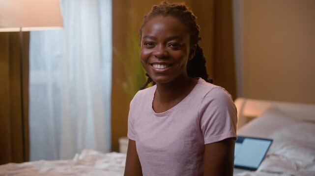 Happy smiling African American woman looking at camera in bedroom at night preparing for sleep at home cheerful female girl relaxing before bedtime enjoy peaceful evening wellness routine rest indoors