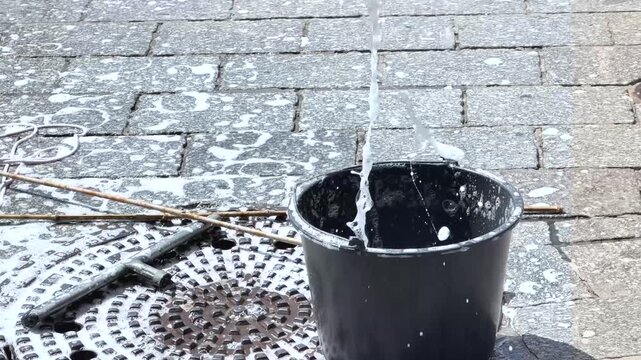 A bubble wand is lifted from a bucket of soapy water, creating large soap bubbles during an outdoor activity on a sunny day.