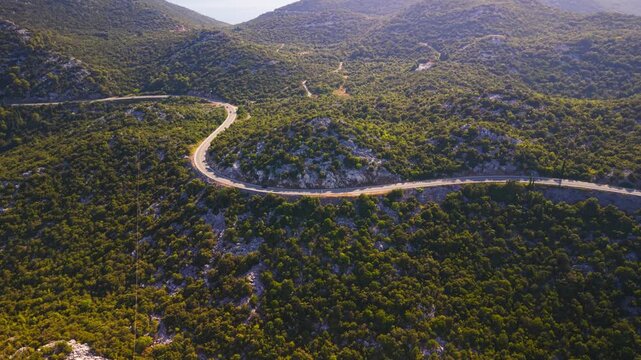 High aerial view of a winding mountain road passing through dense Mediterranean forest near Bacina Lakes and Ploce, Croatia