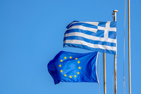 Flags of Greece and European Union fly together against clear blue sky