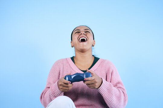 young Latina woman playing video games and holding game controller with copy space on blue background in Mexico Latin America