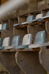 Fototapeta premium A row of numbered molded plastic seats fixed to aged concrete bleachers in an outdoor stadium. Close framing shows seat numbers, muted blue and gray seat