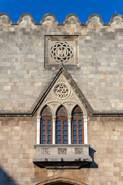 Stone wall with detailed carvings and windows under a clear blue sky during daylight in Rhodes