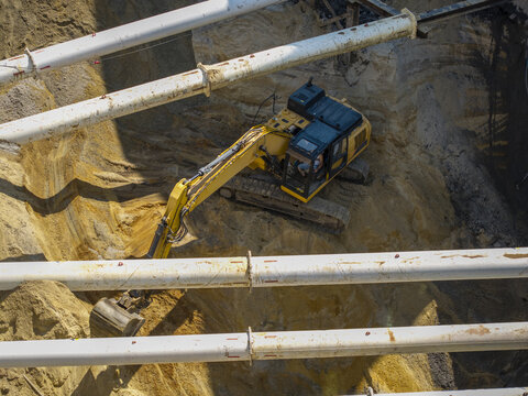 Aerial view of an excavator in a deep construction pit with diaphragm walls and foundation work, surrounded by sandy soil and support pipes in Krakow, Lesser Poland Voivode, Poland.