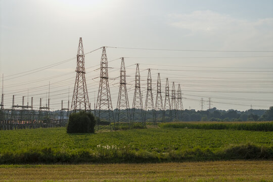 Aerial view of high-voltage electricity pylons and power lines stretching across green agricultural fields in the rural landscape of Poland.