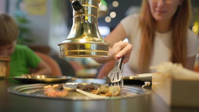Woman grilling seafood at korean barbecue restaurant