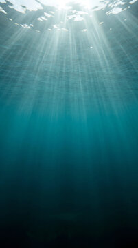Sunlight rays breaking through deep blue ocean water surface, underwater view background.