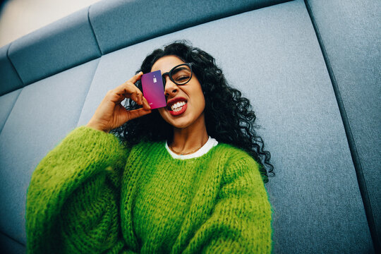 Playful woman student confidently holds credit card for finance and shopping indoors
