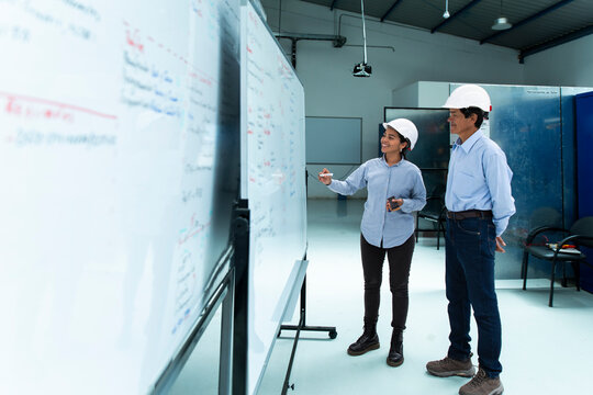 Female engineer explains wind farm strategy to man on whiteboard