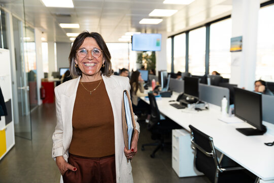 A smiling senior businesswoman holds a folder in a modern office