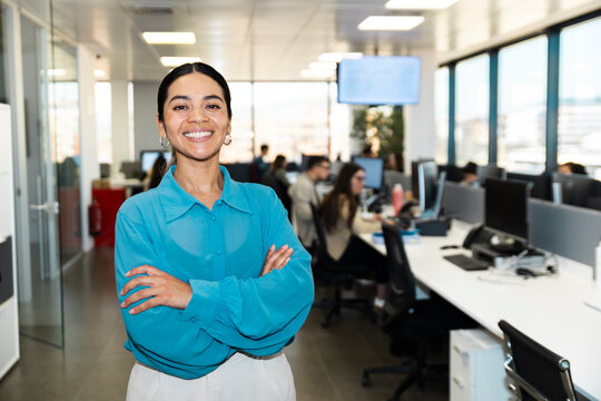 Smiling businesswoman crosses her arms in a modern office workspace