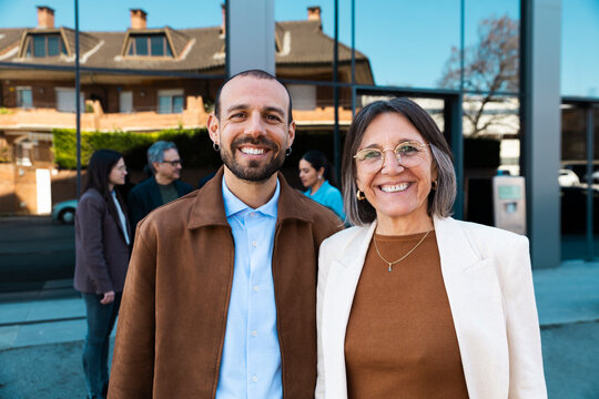 Business partners smile outdoors near a modern office building