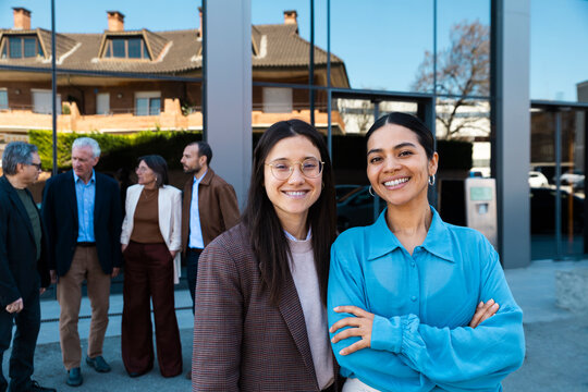 A businesswoman smiles at the camera with her team outside the office