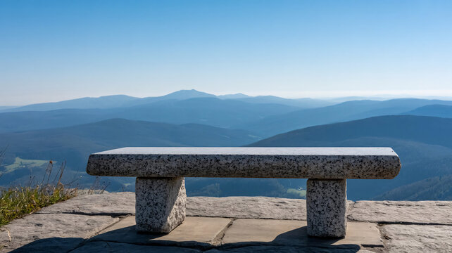 Stone bench sits perfectly positioned on a mountain peak overlooking a vast expanse of blue rolling hills and distant ranges under a bright clear sky, offering a serene place for quiet reflection.