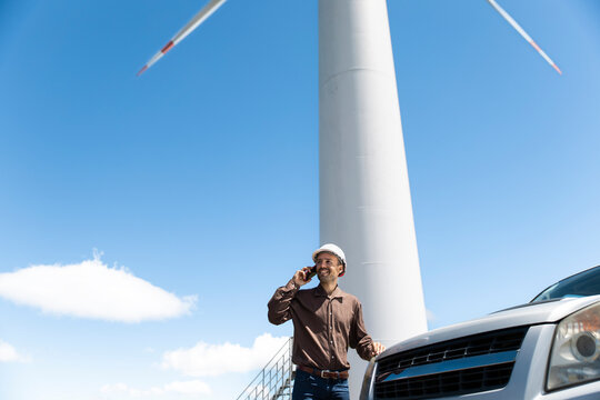 Smiling engineer uses smartphone near wind turbine outdoors in Loja