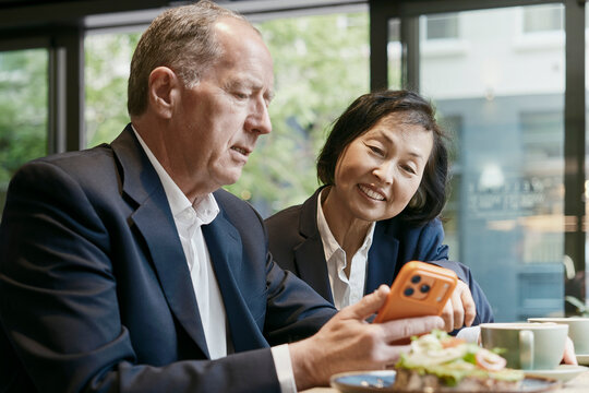 Businessman and businesswoman look at a smartphone during lunch