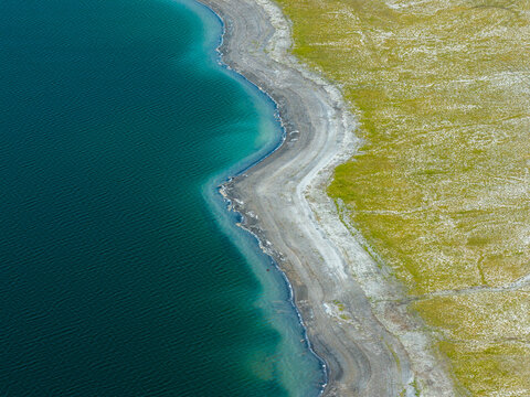 Aerial view of the post-industrial lake featuring turquoise water, a grey gravel shoreline, and vibrant green grassy banks in Poland.