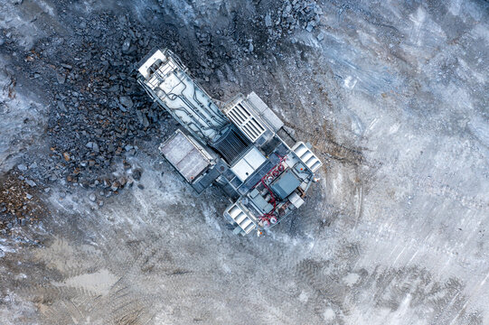 Aerial view of an industrial crusher machine in the Kalksteinbruch Rudersdorf limestone quarry, surrounded by piles of crushed rock and grey earth in Rudersdorf, Brandenburg, Germany.